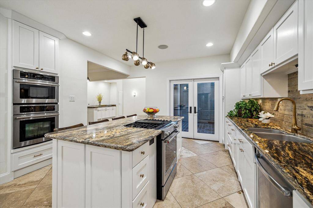 GOURMET ISLAND KITCHEN… Another view of the kitchen that shows the large breakfast bar, stainless undermount sink, dual ovens, and recessed lighting with French door access to private courtyard.