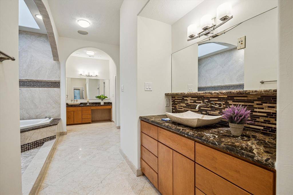 PRIMARY BATHROOM… This view provides a view of the dual travertine vessel sinks, custom cabinetry, separate vanity seating area and large mirrors.  Each vanity area has its own array of cabinetry.