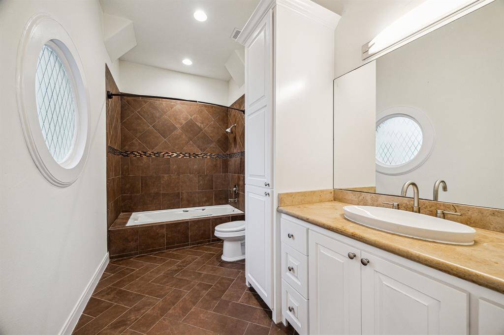 ENSUITE BATHROOM… Tile flooring, marble counter and backsplash with ceramic vessel sink, vanity lighting, built-in cabinetry, tub/shower with tile surround and decorative tile inlay.