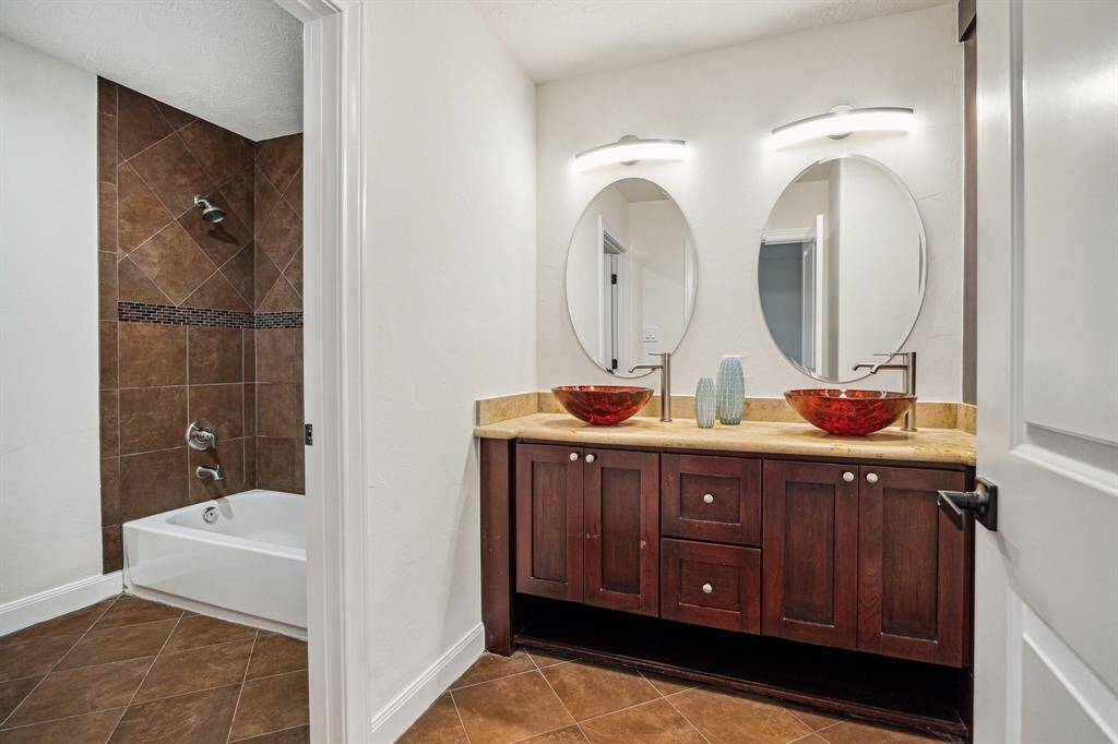 ENSUITE BATHROOM… Tile flooring, marble counter and backsplash with custom glass vessel sinks, vanity lighting, beveled mirrors, built-in cabinetry, tub/shower with tile surround and decorative tile inlay.
