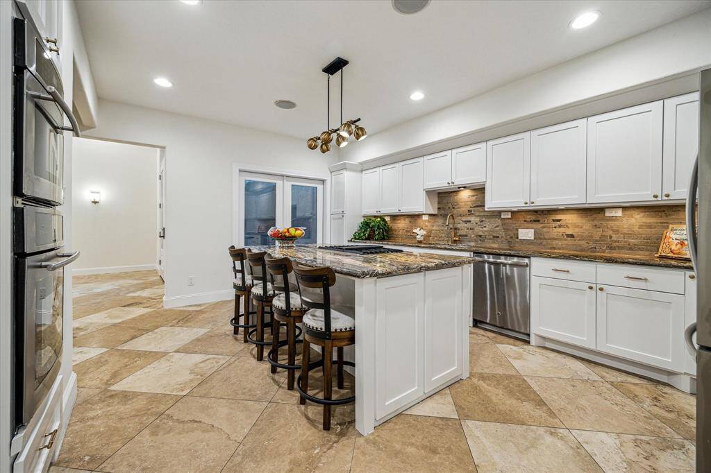 GOURMET ISLAND KITCHEN… Granite counters and a four-stool-island provide abundant counterspace. Features travertine backsplash and floors, dual ovens, gas cooktop, plentiful cabinets, two walk-in pantries and a private kitchen courtyard.