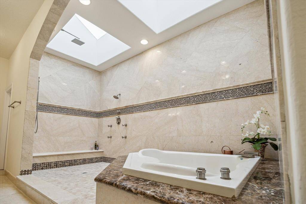 PRIMARY BATHROOM… The lavish primary bath opens up into a Romanesque vaulted space that feels like your own private spa. Three large skylights make additional lighting redundant on most days and moonlit nights. The vast frameless wet room has seven shower heads on two walls, including a rain shower. Marble bench seating follows the length of the shower.