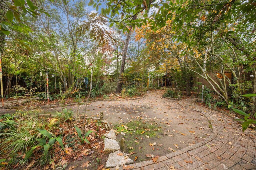 The backyard with winding stone paths, lush greenery, and mature trees providing a serene, natural setting.