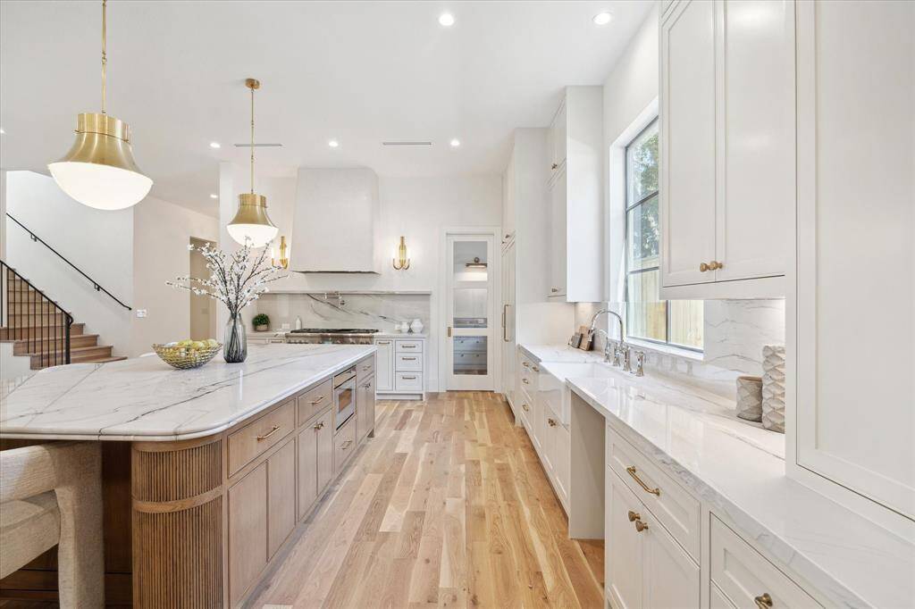 The kitchen island features a Quartzite countertop with double bullnose edge, white oak reeded details, and plenty of storage! The kitchen vent-hood is completed with a plaster finish and brass sconces on each side.