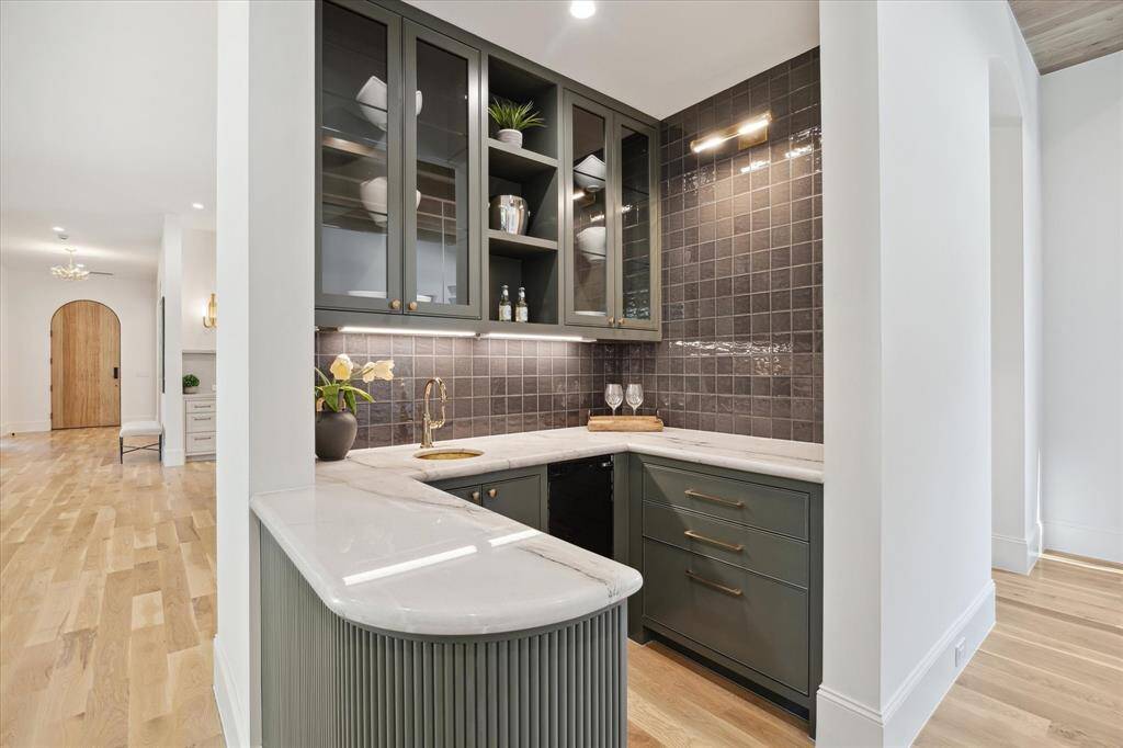 The wet bar with brass fixtures and sink, ice maker, glass cabinetry, counter to ceiling tile and reeded details. No details were missed in completing this space!