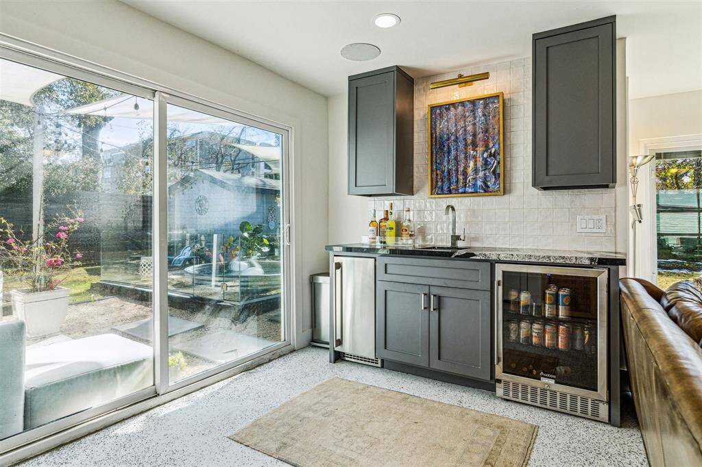 The wet bar features granite counters, Zellige tile backsplash, stainless steel sink. a beverage cooler and space for an ice maker.