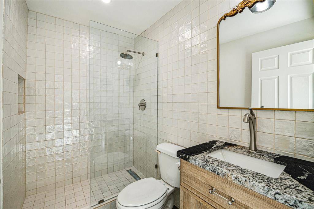A full bath completes the space in the guest suite and includes a walk-in shower with Zellige tile surround, natural wood cabinet with granite counter, recessed lighting, and vanity lighting.