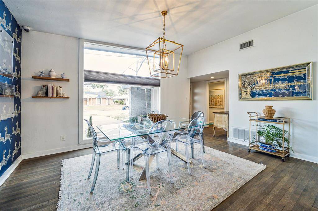 The sun filled, formal dining room overlooks the front yard through a wall of windows and features hardwood floors, designer chandelier, vaulted ceiling, and an accent wall with designer wallpaper.