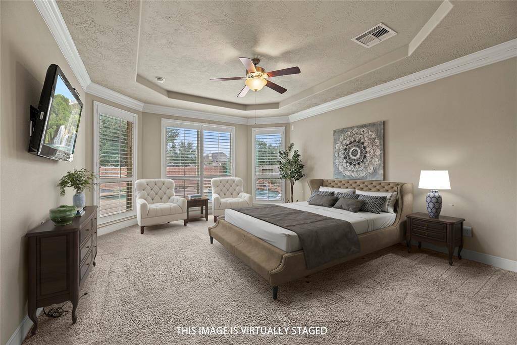 Spacious primary bedroom featuring elegant crown molding and a stunning tray ceiling, creating a serene and sophisticated retreat