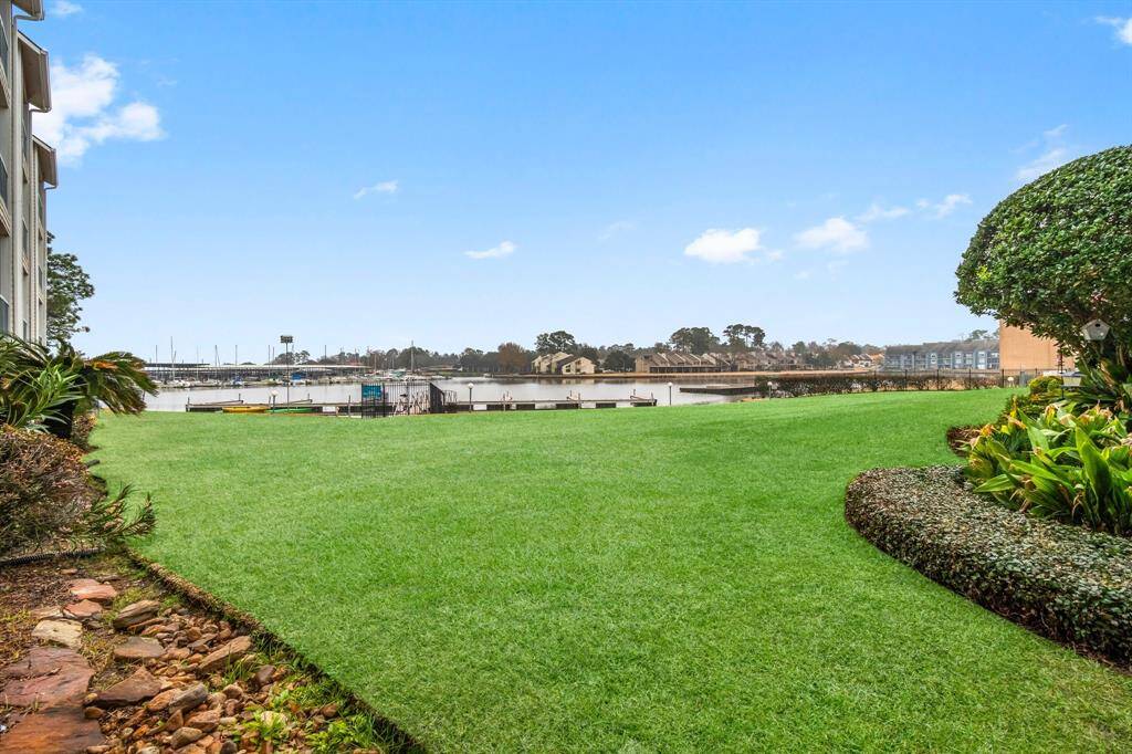 Spacious, well-maintained lawn with a view of a marina and water, bordered by neatly trimmed shrubs and plants, offering a serene and picturesque setting.