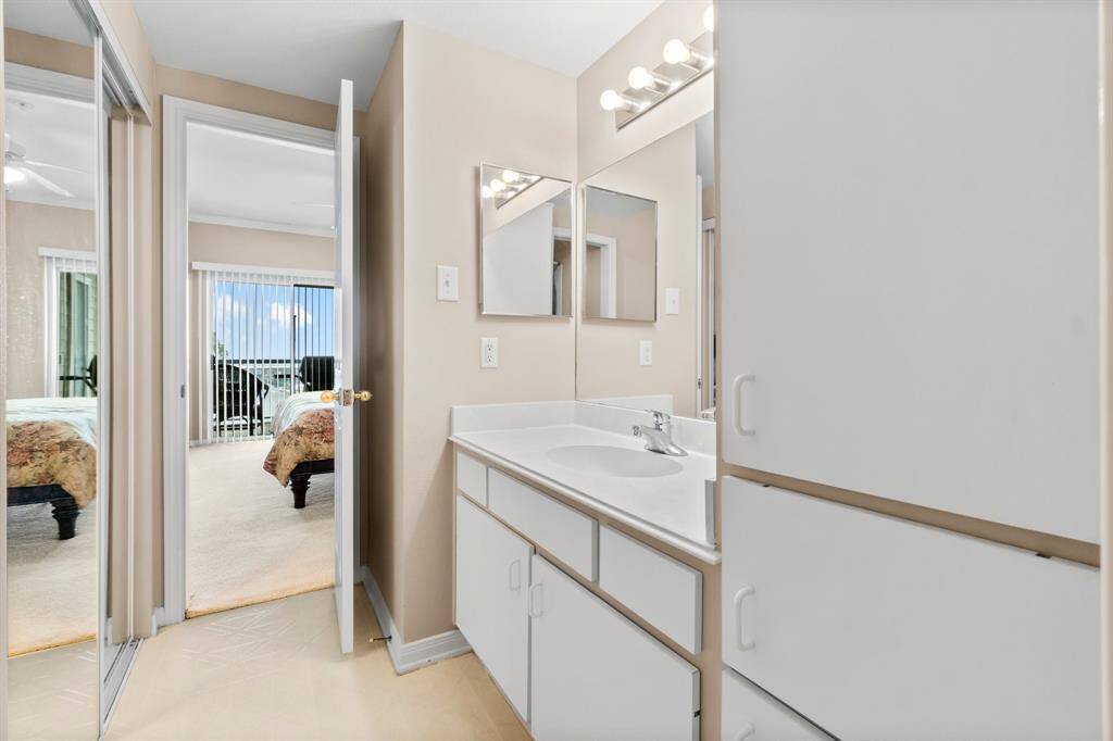 bright bathroom with a large mirror and vanity, leading into the primary bedroom with a sliding glass door that opens to a balcony with a view.