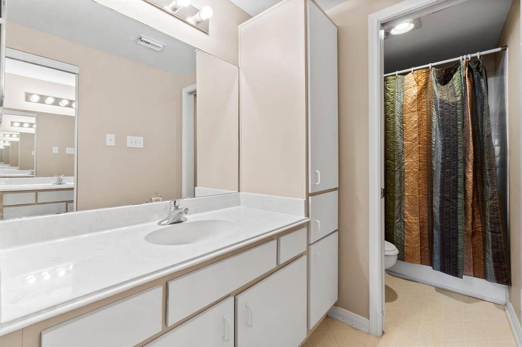 This bathroom features a sleek vanity with ample storage, a large mirror, and contemporary lighting. It includes a shower with a colorful curtain, offering a functional and stylish space.