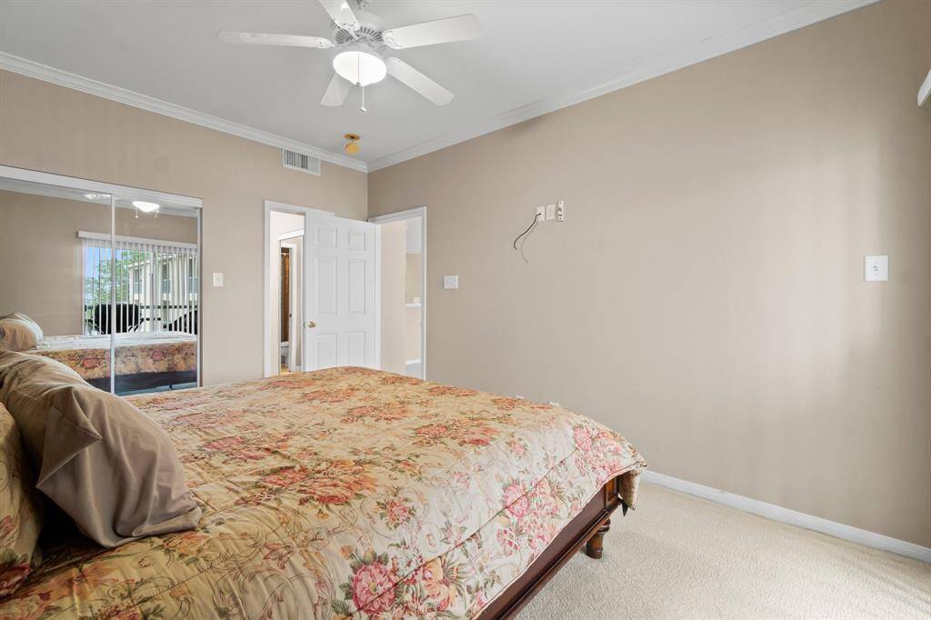 Primary bedroom features a cozy space with neutral walls and carpet, a ceiling fan, mirrored closet doors, and ample natural light.