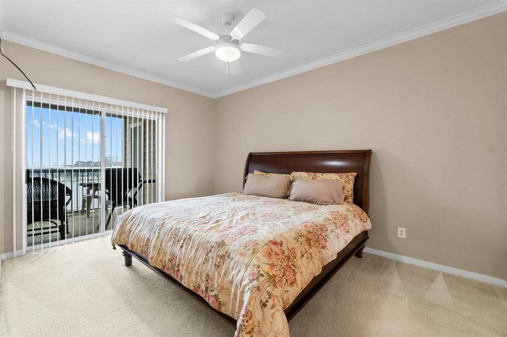 Primary bedroom features a large bed, neutral walls, and a ceiling fan. It opens to a balcony through sliding glass doors, providing natural light and a view, perfect for relaxing.