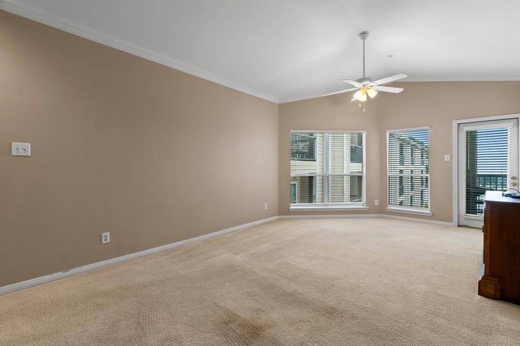 Spacious living room with neutral walls and carpet, featuring large windows for natural light, a ceiling fan, and access to a balcony.