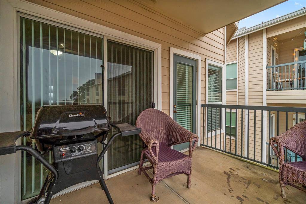 Cozy balcony with space for seating and a grill, featuring sliding glass doors and a view of neighboring buildings. Perfect for outdoor relaxation and entertaining.