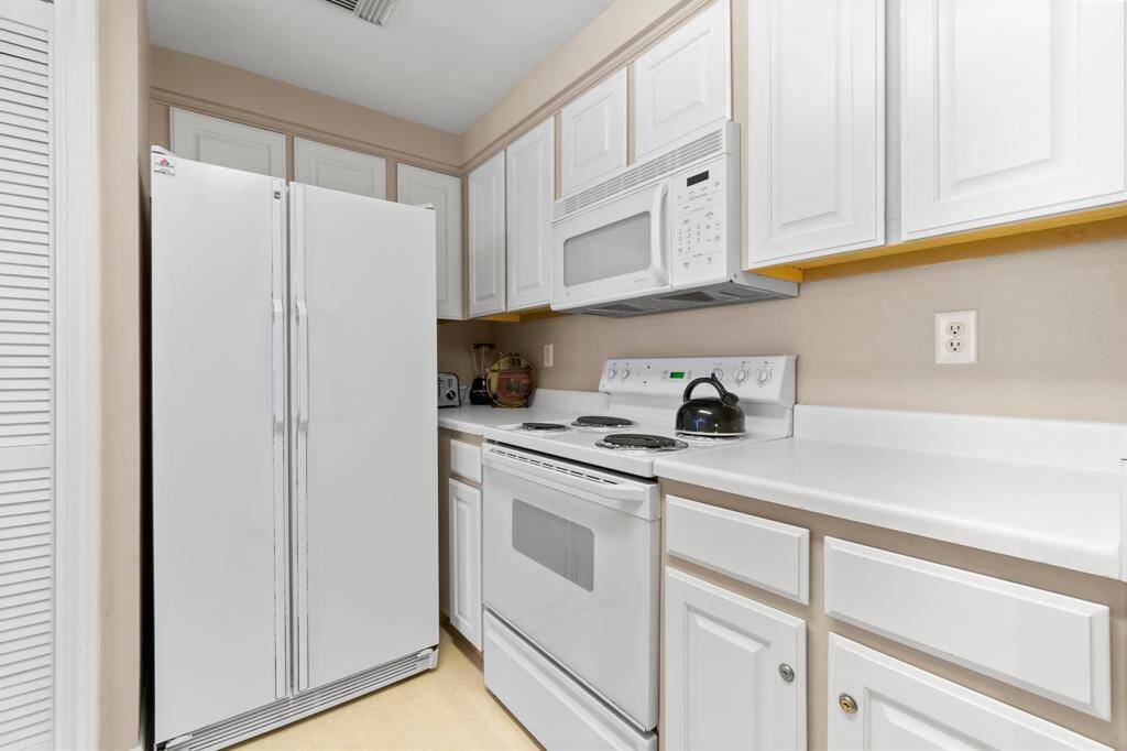 This kitchen features white cabinetry and appliances, including a refrigerator, stove, and microwave. The countertops are spacious, creating a clean and functional workspace.