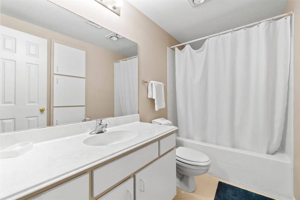 This bathroom features a clean, minimalist design with a white vanity and sink, a bathtub with a shower curtain, and neutral-colored walls. It includes built-in storage cabinets and a modern light fixture, providing functionality and style.