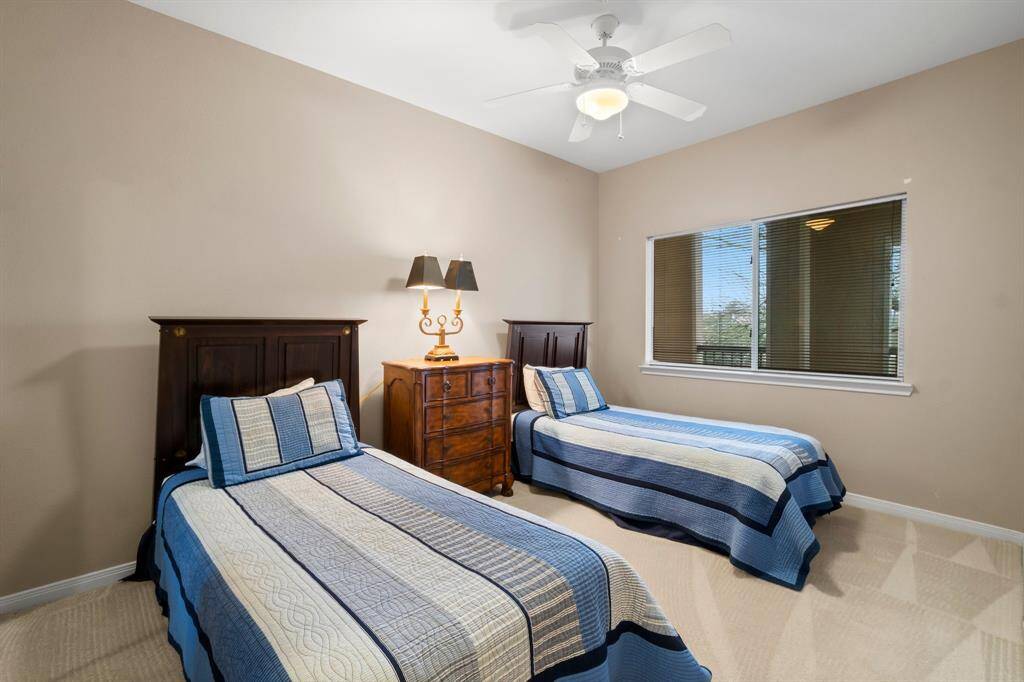 2nd bedroom features two twin beds with matching striped bedding, a wooden nightstand with a lamp, and a ceiling fan. The room is well-lit with a large window offering natural light.