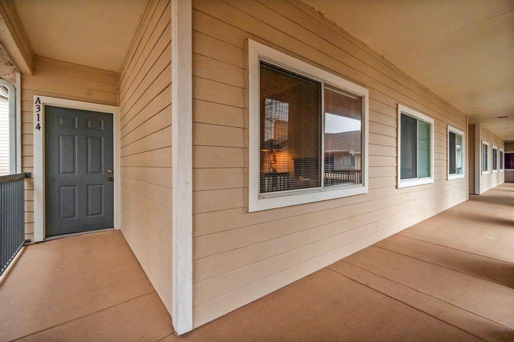 exterior hallway of the complex, featuring a clean, covered walkway with beige siding and large windows. The entrance to unit A314 is highlighted by a dark gray door with a white frame.