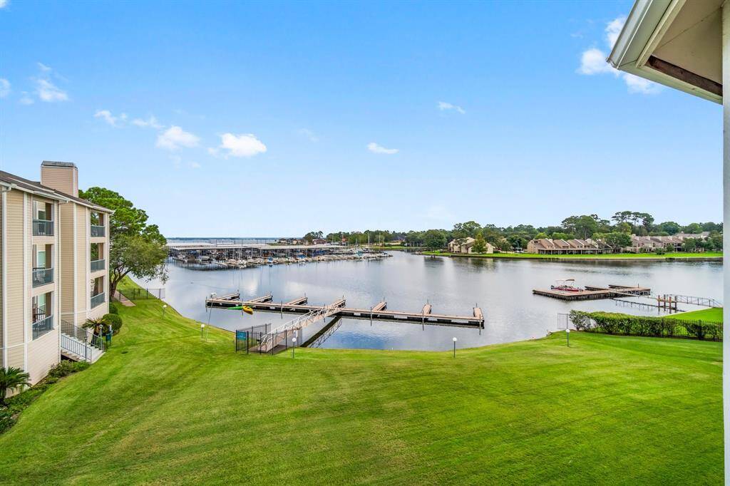 serene waterfront view from a residential property. It features a well-maintained grassy area leading to a dock with boat slips.