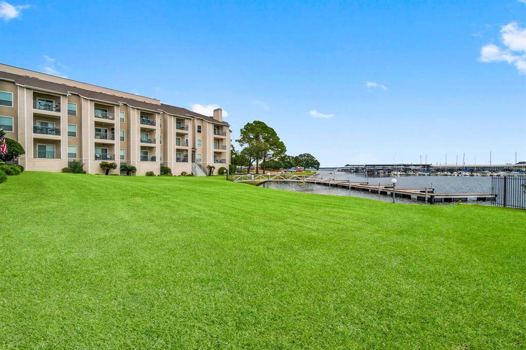 waterfront condominium complex with a well-maintained lawn leading to a dock. The building features multiple balconies, offering scenic views of the water and marina. Ideal for those seeking a relaxing, lakeside lifestyle.