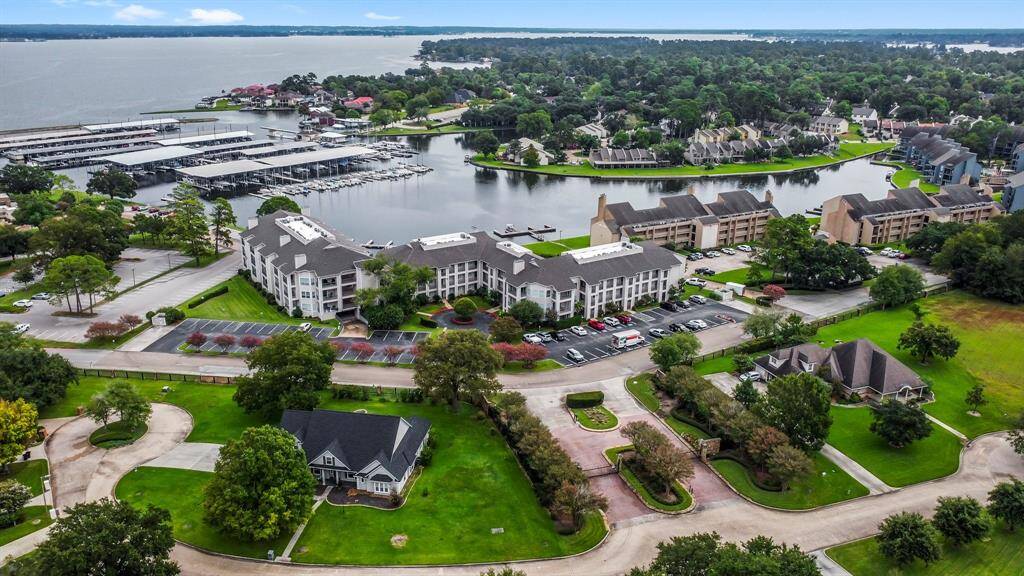 a picturesque waterfront community with modern buildings and homes surrounded by lush greenery. A marina with numerous boats, and the area offers serene water views, making it an attractive location for those seeking a blend of nature and convenience.