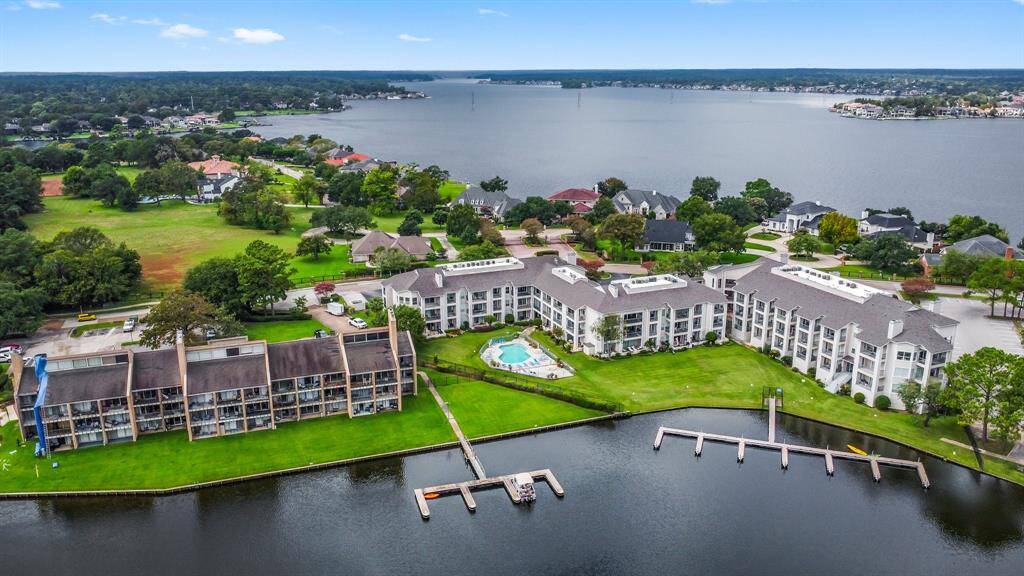 waterfront property with modern condominiums overlooking a scenic lake. The complex features well-maintained green lawns, a central swimming pool, and private docks. The surrounding area is lush and residential, offering a peaceful and picturesque setting.