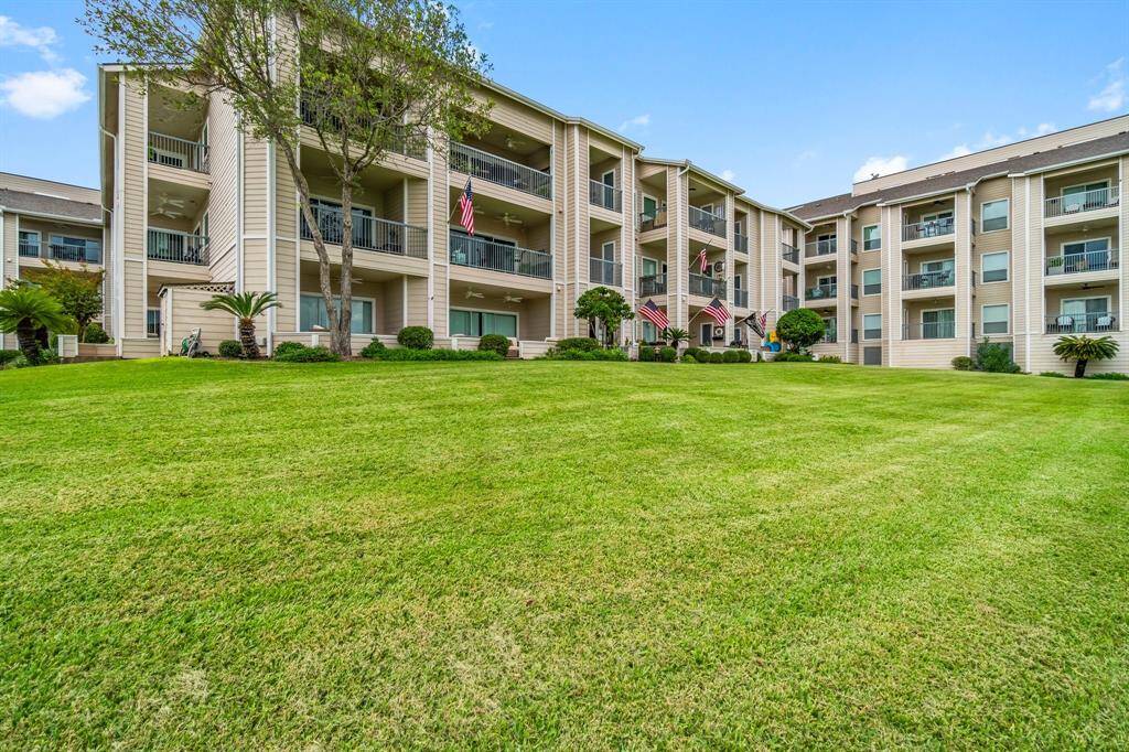 This photo showcases a well-maintained complex with multiple stories, featuring balconies and surrounded by lush green lawns. The buildings have a clean, modern design, with flags displayed at the entrance, creating an inviting atmosphere.