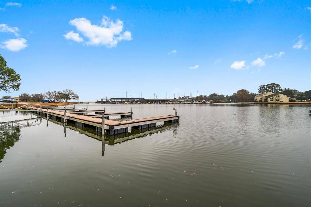 serene waterfront view with a wooden dock extending into calm waters, ideal for boating enthusiasts. The surrounding area includes trees and residential buildings, offering a peaceful, scenic setting.