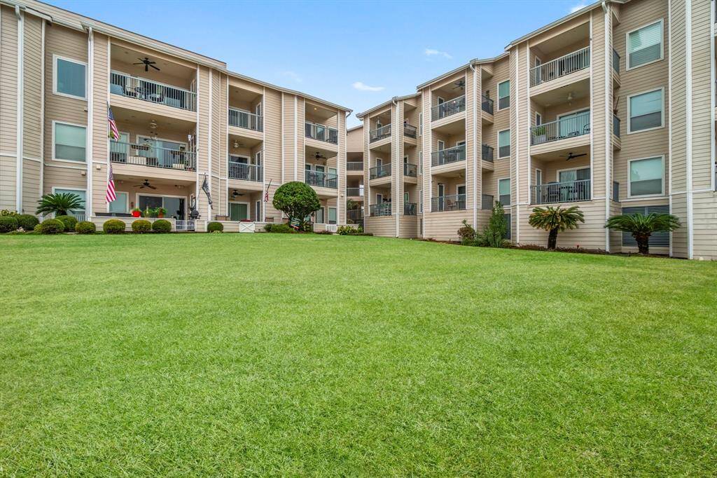 well-maintained Comdo complex with three stories, featuring balconies and a large green lawn. The building is surrounded by manicured shrubs and small trees, offering a neat and welcoming exterior.