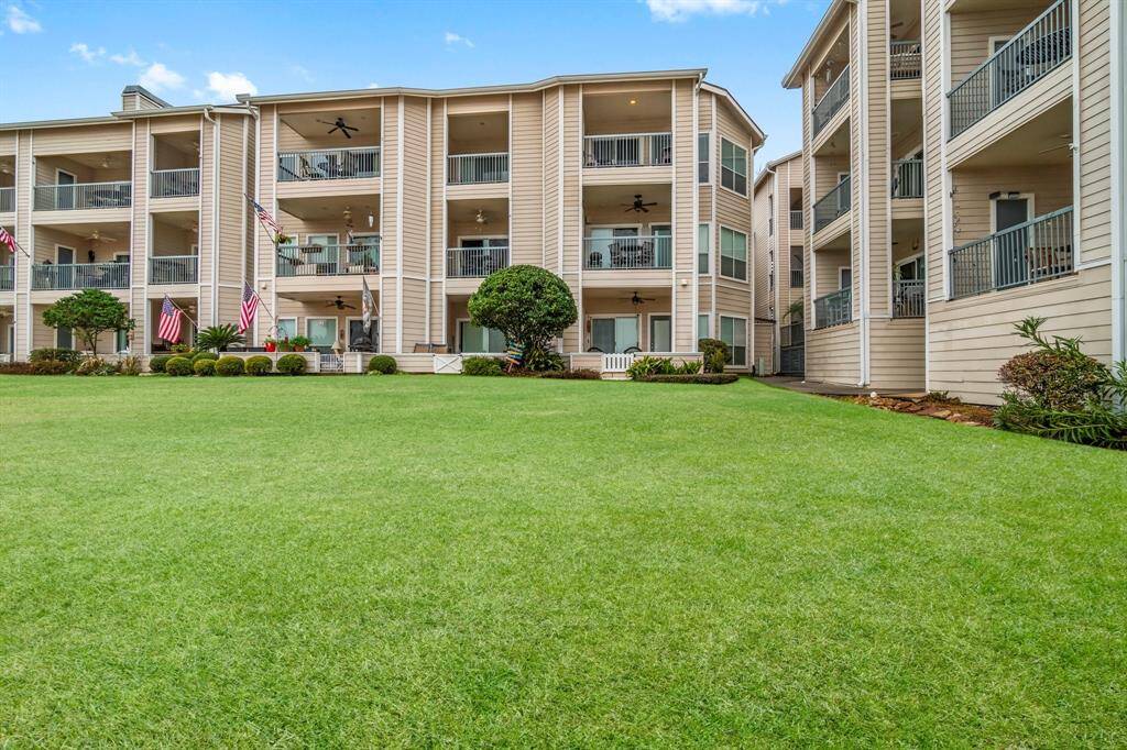 multi-story apartment building with spacious balconies and a well-maintained lawn. The siding is neutral-toned, and there are decorative plants and American flags enhancing the exterior. The setting is peaceful and inviting.