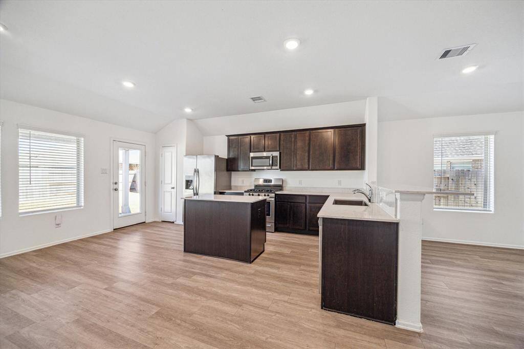 This photo showcases a spacious, open-concept kitchen with modern dark wood cabinetry and stainless steel appliances