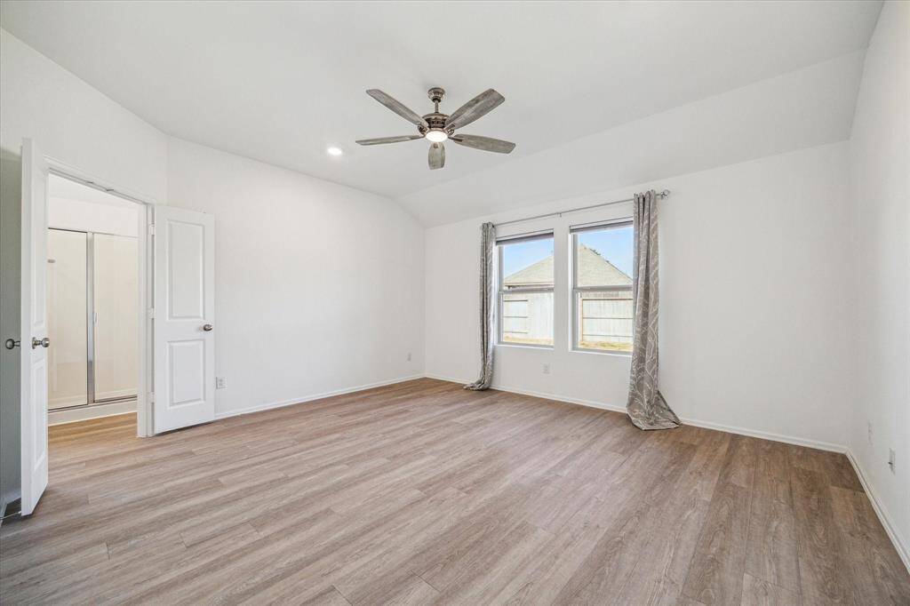 This spacious primary bedroom features sleek wood laminate floors and ample natural light.