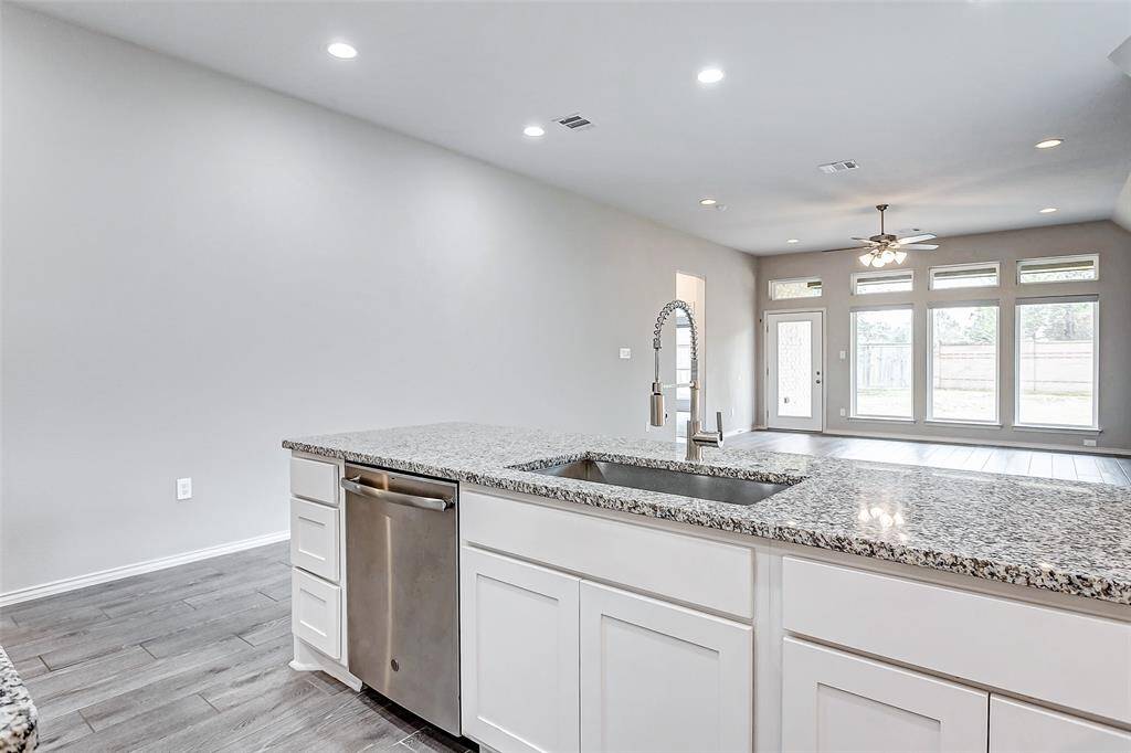 Open-concept kitchen features a large granite island with a stainless steel sink and dishwasher and undermount sink.
