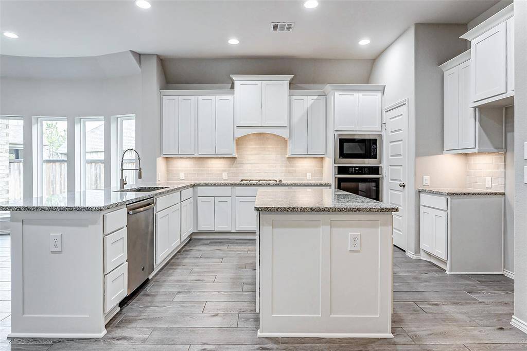 This modern kitchen features sleek white cabinetry, granite countertops, and stainless steel appliances. It includes a spacious island, ample storage.