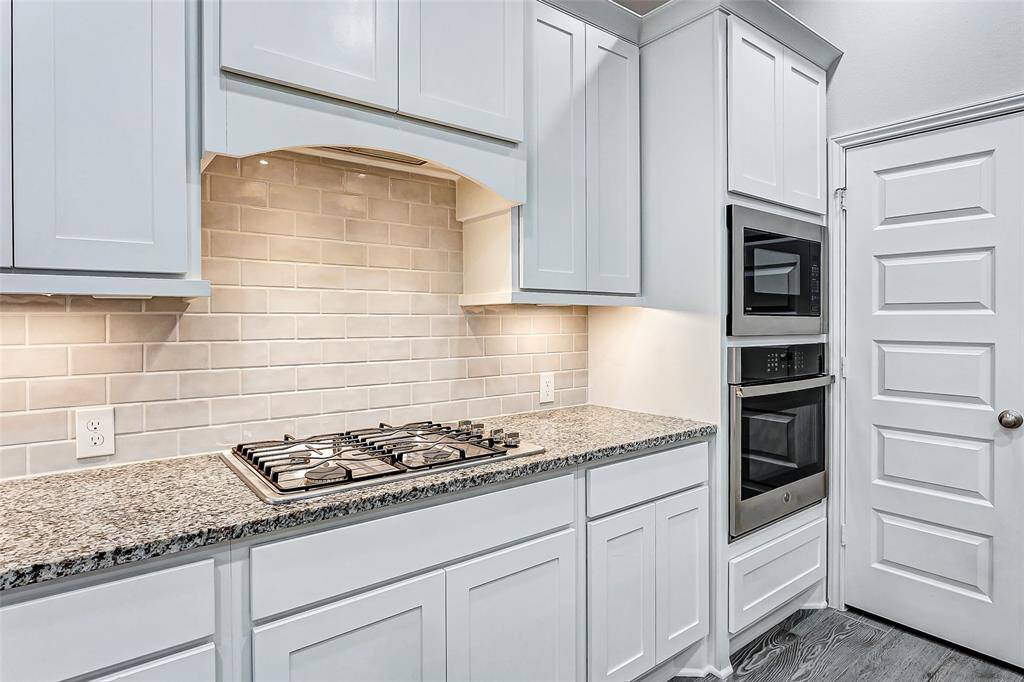 This modern kitchen features a gas cooktop, and stacked stainless steel ovens. The light subway tile backsplash adds a bright, clean touch.