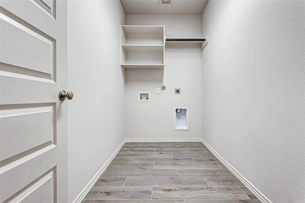 This is a utility room with light-colored walls and tile flooring. It features built-in shelving, a hanging rod, and connections for a washer and dryer.
