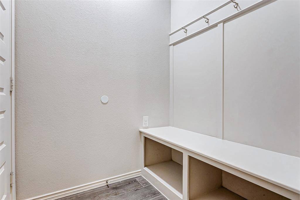Mudroom with a built-in bench featuring storage cubbies underneath. There are wall hooks above for hanging items, and the space has a modern, minimalist design with neutral colors.