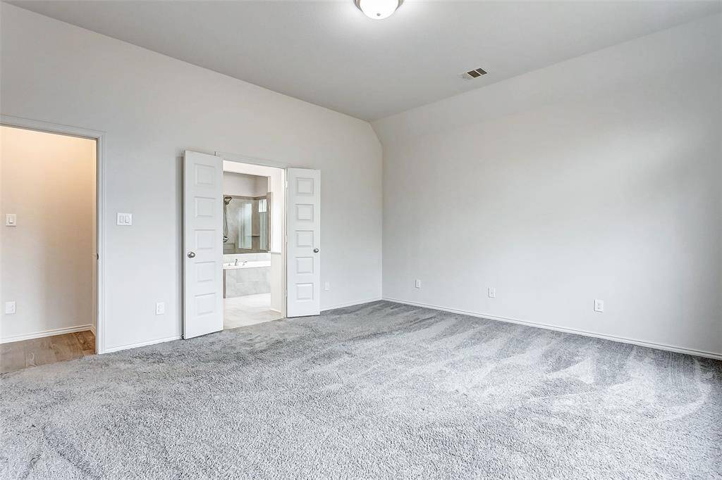 Spacious bedroom with neutral walls, plush carpet, and a ceiling light. Features double doors leading to an ensuite bathroom, offering a modern and inviting space.