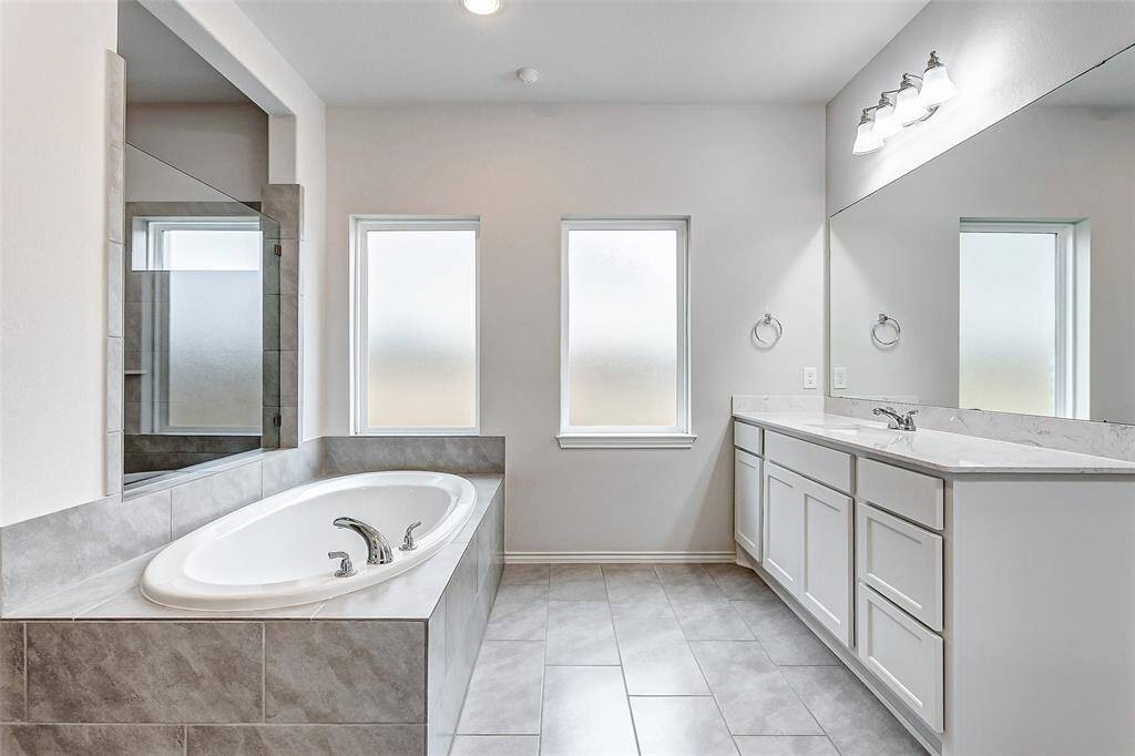 Spacious soaking tub, a large vanity with dual sinks, and ample natural light from two frosted windows. The neutral tile flooring and sleek fixtures create a clean, elegant look.