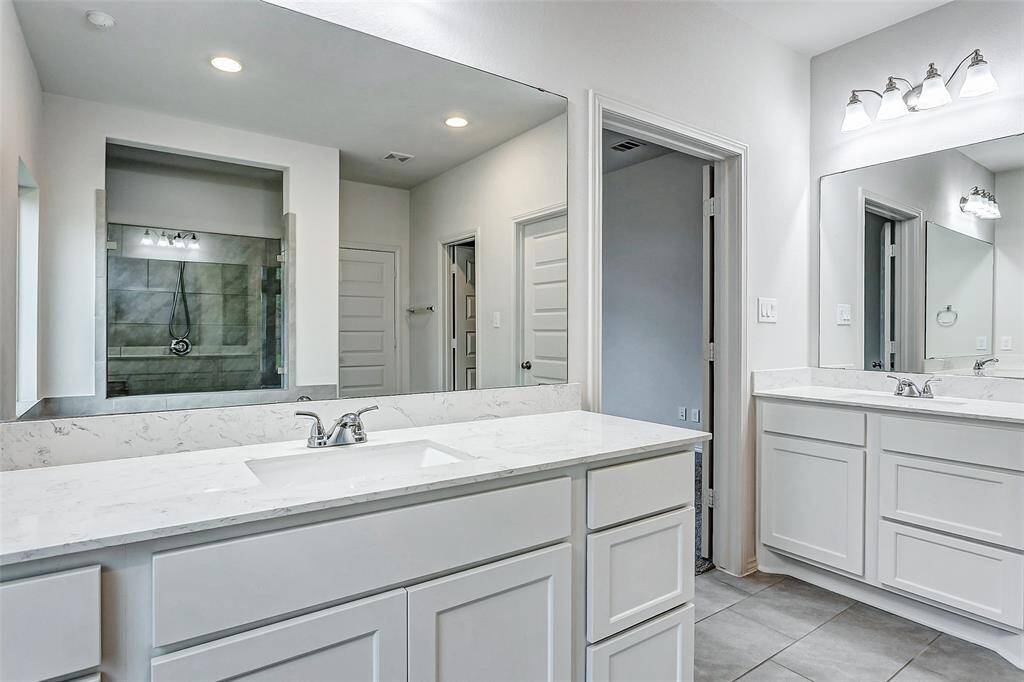 This bathroom features a modern design with dual sinks, white cabinetry, and a spacious walk-in shower.