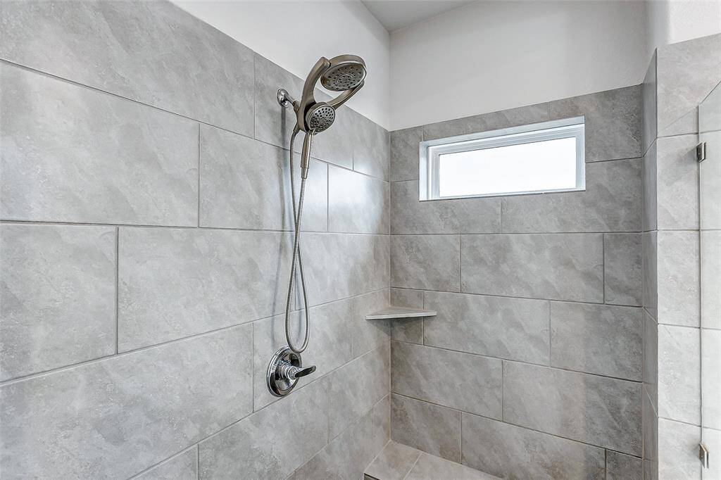 Modern shower with large gray tiles, a sleek showerhead, and a small built-in shelf. A bright window provides natural light.
