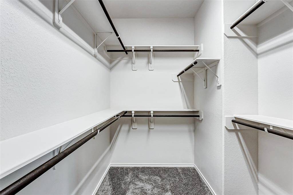 Spacious walk-in closet with multiple shelves and hanging rods, offering ample storage space. The walls are painted white, and the flooring is carpeted, creating a clean and organized look.