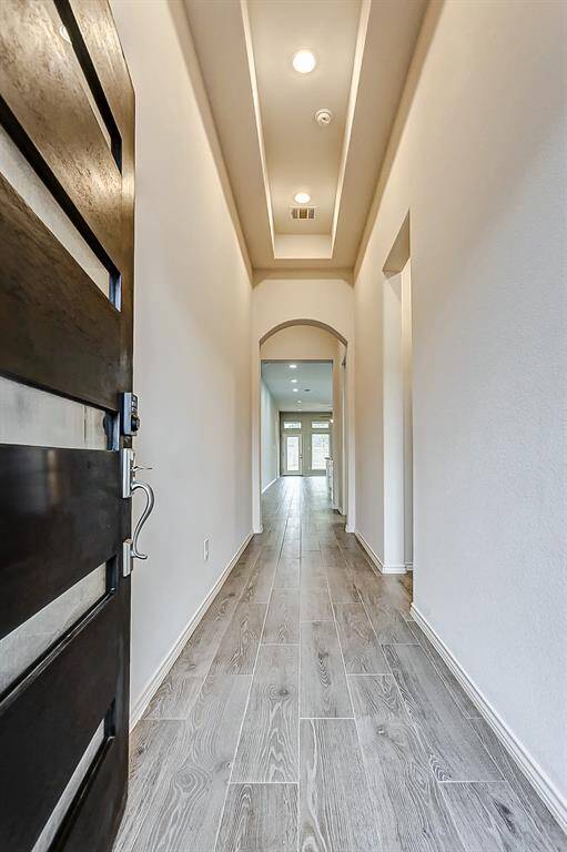 Inviting entryway with sleek, light-color wood flooring and high ceilings with recessed lighting. The hallway leads to a bright living area, creating a spacious and welcoming atmosphere.