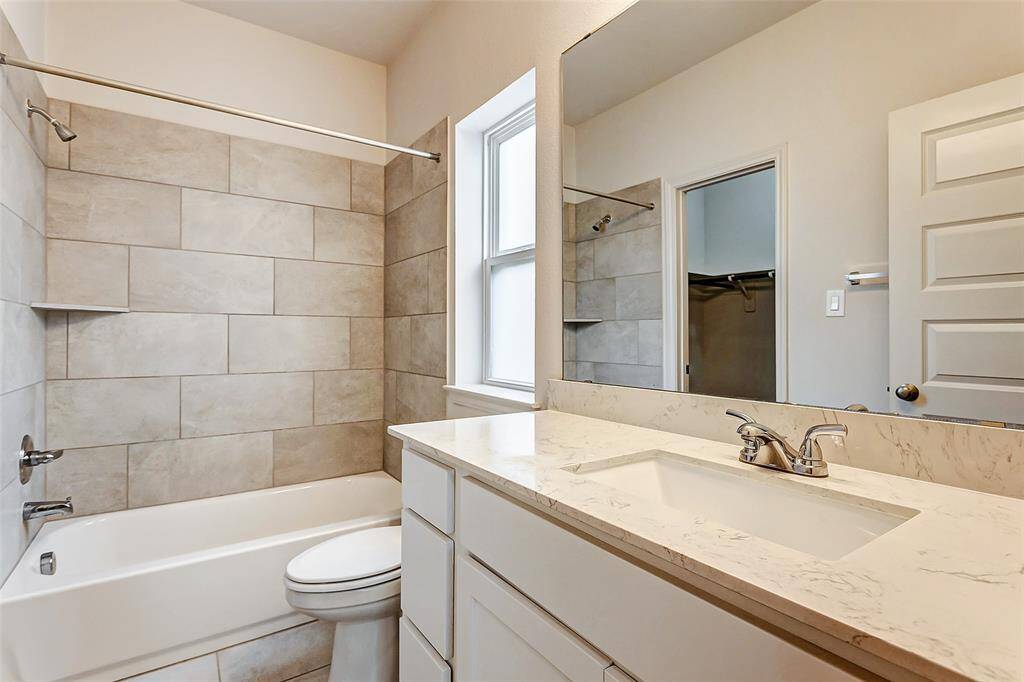 Bathroom features a modern design with a large vanity and marble countertop. It includes a bathtub with beige tile surround, a window for natural light, and a spacious mirror above the sink.