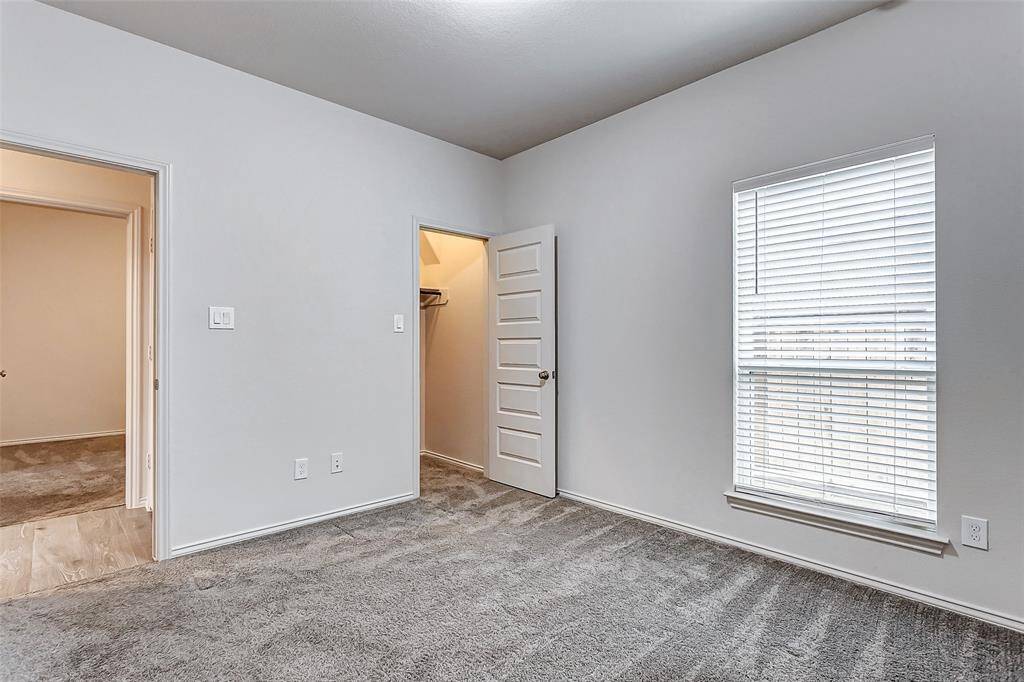 This room features a neutral color palette with carpeted flooring, a window and a spacious closet with a paneled door.