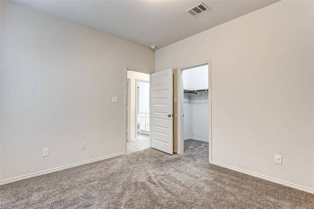 A simple, carpeted bedroom with neutral walls and an open door leading to a walk-in closet.