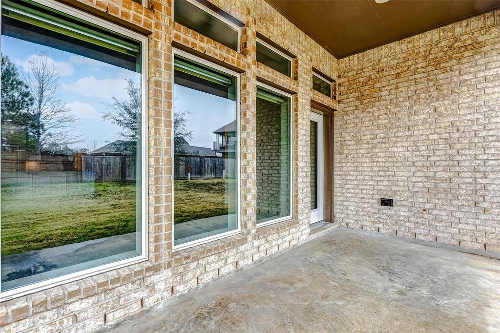 Covered patio with large windows overlooking a spacious backyard. The brick walls and concrete floor offer a durable and low-maintenance outdoor space, ideal for relaxation or entertaining.