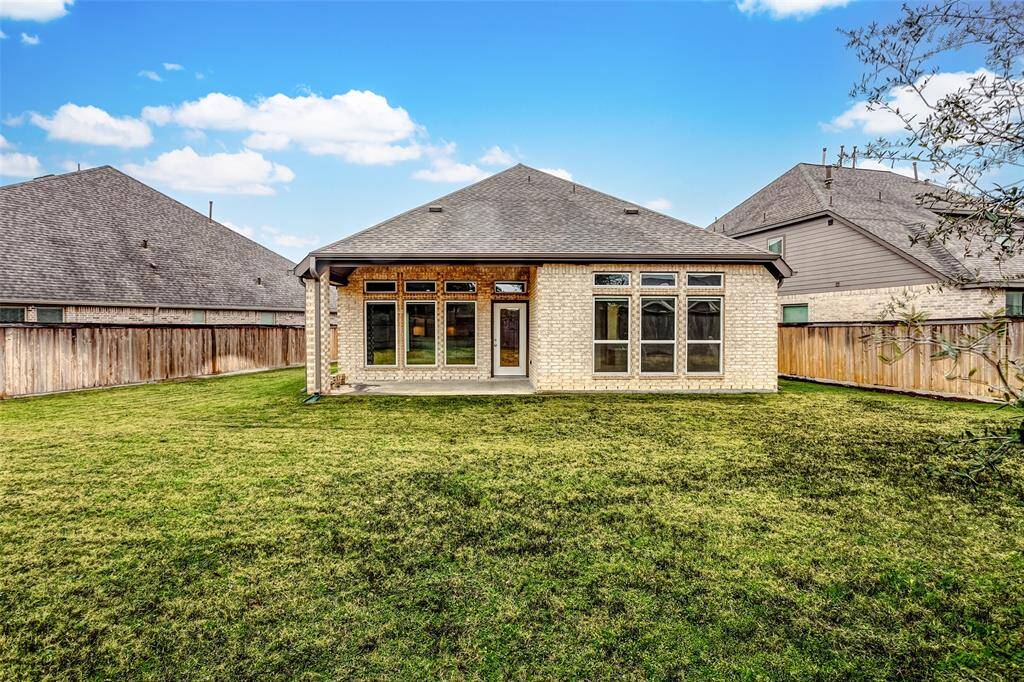 The backyard with a spacious grassy area and a wooden fence for privacy. Large windows offer plenty of natural light.